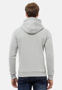 Helles graues Hoodie mit Kapuze und Kordelzug, gerippten Bündchen und Saum, aus weichem Stoff. Das Rückendesign ist einfach und nahtlos. Getragen mit blauen Jeans.