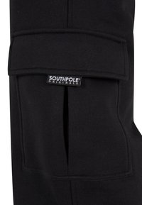 Czarne dresy z kieszenią na przodzie i klapką. Wykonane z miękkiego materiału, mają naszywkę z logo "SOUTHPole Originals."