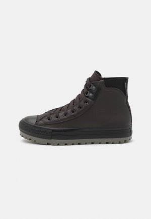 Zapatilla de alta negra hecha de cuero liso con una suela de goma texturizada, con ojales de metal y acentos en gris contrastante.