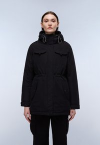 Sort parka-jakke med hætte, justerbare snore, sidelommer og knapdetaljer. Fremstillet af et holdbart, tekstureret stof.