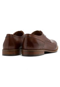 Brązowe skórzane buty odświętne o gładkim wykończeniu, zaokrąglonym nosku i drewnianej podeszwie. Charakteryzują się minimalnym szyciem i eleganckim, gładkim designem.