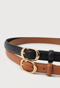 Δύο δερμάτινες ζώνες, μία μαύρη και μία καφέ, κάθε μία με μια χρυσή αγκράφα σε σχήμα οβάλ, ξαπλωμένες θεαματικά σε λευκό φόντο.