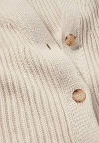 Beige Rippenstrickjacke mit strukturiertem Strick, rundem Halsausschnitt und kontrastierenden hellbraunen Knöpfen mit vier Löchern.