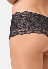 Zwarte kanten string met bloemenpatroon, gegolfde randen en een doorschijnende textuur. Ontworpen voor een aansluitende pasvorm.