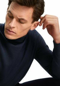 Navyfarbener Rollkragenpullover aus einem weichen, strukturierten Strick. Enganliegendes Design mit hohem Kragen. Das Model hat kurze braune Haare und einen neutralen Gesichtsausdruck.