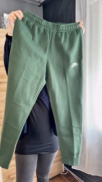 Zelené nohavice Nike so širokým elastickým pásom a bielym logom. Vyrobené z mäkkej tkaniny s voľným strihom, ktorý zobrazuje hladkú textúru.