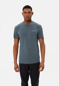 Grijze T-shirt met korte mouwen en een ronde halslijn, voorzien van een klein wit logo op de linkerkant van de borst, gecombineerd met zwarte broek. Zachte stofstructuur.