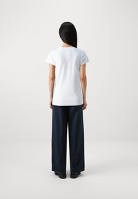 Camiseta blanca de manga corta con escote redondo, combinada con pantalones de pierna ancha en color marino, vista desde atrás, sobre un fondo claro y liso.