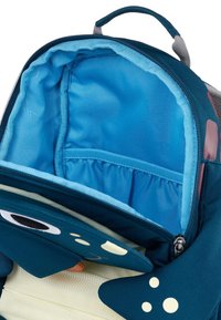 Interno di uno zaino di tessuto teal con fodera azzurro chiaro, dotato di una tasca con zip e tasche laterali elastiche. Include accenti di design giocosi.