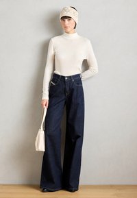 Bredde jeans i mørk denim parret med en tætsiddende cremefarvet turtleneck. Tilbehøret inkluderer et mønstret hårbånd og en lille beige håndtaske.