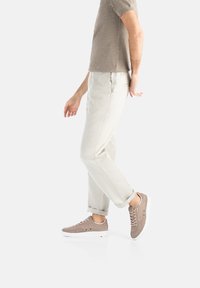 Beżowe casualowe spodnie w połączeniu z brązowymi zamszowymi trampkami z białą podeszwą. Strój dopełnia jasnobrązowa koszula z krótkim rękawem.