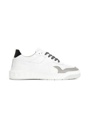 Hvid sneaker med lavt snit med sort hælflap, grå detaljer nær tåen og sort-hvide mønstrede snørebånd på hvid sål.
