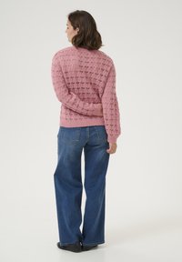 Maglione rosa lavorato a maglia con un motivo testurizzato, vestibilità rilassata e polsini a coste, abbinato a jeans a gamba larga blu e scarpe nere.