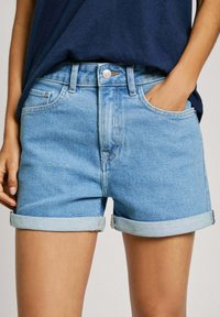 Ljusblå denimshorts med upprullade fållar, femfickorsdesign och knappstängning framtill. Slät textur och klassisk passform.