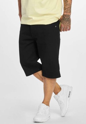Svart denimshorts med rå kant, med sidelommer og en liten stretch. Kombinert med hvite sneakers som viser et rent design.