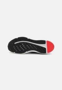 Semelle en caoutchouc noire avec une surface texturée. Dispose d'un intercalaire blanc et d'un accent rouge au niveau du talon pour une meilleure traction et stabilité.