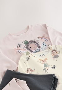 Deux vêtements pour enfants sont exposés : un sweat-shirt rose avec des illustrations et un haut crème avec des motifs. Un tissu gris foncé est également inclus.