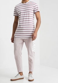 Randig kortärmad t-shirt i ljusrosa och vit, kombinerad med ljusrosa tapered byxor med en vit logodetalj på sidan.