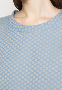 Světle modrý pletený top s texturovaným vzorem v béžové barvě, s kulatým výstřihem a měkkou, prodyšnou tkaninou.