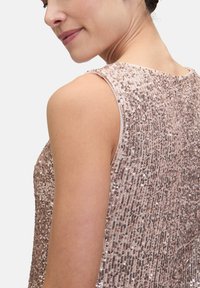 Top bez rękawów wykonany z jasnoróżowej tkaniny pokrytej pionowymi rzędami małych, błyszczących cekinów. Posiada okrągły dekolt i subtelną teksturę.