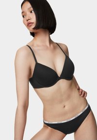 Soutien-gorge nero con un design triangolare liscio e sagomato, spalline regolabili. Abbinato a mutandine nere coordinate con una banda elastica bianca con l'etichetta "BODY".