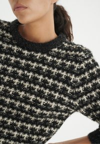 Pull en maille texturée noir et crème avec une finition duveteuse, doté d'un col rond et d'un motif pied-de-poule.