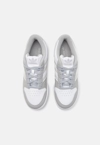 Zapatillas deportivas blancas y grises con una parte superior de cuero suave, cuello acolchado, lengua de malla y caja de dedos perforada. Presenta tres rayas blancas.