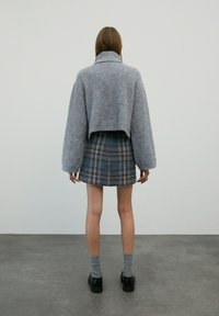 Grauer, kurzer Strickpullover mit weitem Kragen und lockeren Ärmeln, kombiniert mit einem blauen karierten Miniröcken und grauen gerippten Socken. Schwarze Schuhe getragen.