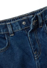 Vaqueros de mezclilla con un lavado azul oscuro, con cierre de botón de metal, trabillas para el cinturón y detalles de costura visibles en los bolsillos y costuras.