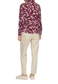 Lange mouwen shirt in kastanjebruin met lichtpaarse bladdessin; gecombineerd met crèmekleurige tapered broek en witte sneakers met beige accenten.
