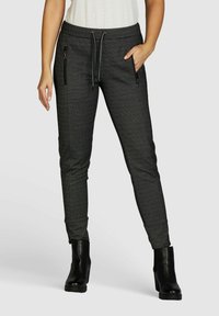 Joggings grisés fuselés avec des poches zippées sur les côtés, une taille élastiquée avec cordon de serrage et un tissu texturé. Associés à des bottines noires.