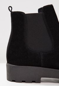 Botte Chelsea en daim noir avec panneau latéral élastique, languette de tirage et semelle crantée épaisse.