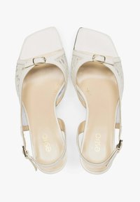 Białe sandały na obcasie z kwadratowym noskiem, z ozdobnym sznurowaniem i paskiem na klamrę. Wkładka jest w jasnym beżu z wytłoczonym logo.