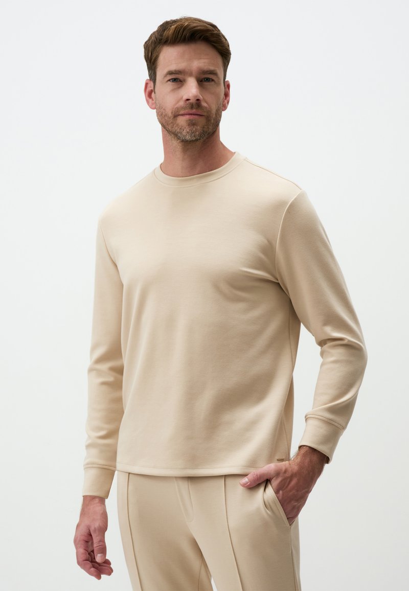 Camicia beige a maniche lunghe in tessuto morbido con scollatura rotonda, dotata di polsini a costine e vestibilità comoda, abbinata a pantaloni beige coordinati.