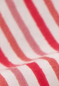 Detailný záber na textíliu s diagonálnymi červenými a oranžovými pruhmi na bielom pozadí, zobrazujúci textúru a tkaný vzor.