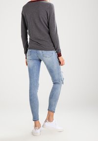 Pull gris avec une bordure bordeaux au niveau du col, associé à un jean skinny bleu clair déchiré et des baskets blanches. Look propre et décontracté.