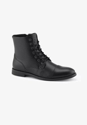 Botas de tobillo de cuero negro con acabado texturizado, que cuentan con ojales de metal, diseño de cordones, punta redondeada y suela plana de goma.