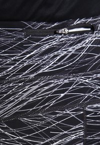 Černé sportovní legíny s bílým abstraktním vzorem, elastický materiál, kapsa na zip a kontrastní švy.