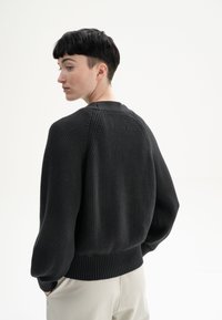 Chunky schwarzer Pullover mit strukturiertem Strick, gerippten Bündchen und Saum sowie Rundhalsausschnitt. Die Rückansicht zeigt überschnittene Schultern und Nahtdetails.