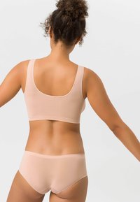 Leichte, gerippte Stoff-Bralette in sanftem Beige mit breiten Trägern; kombiniert mit passenden nahtlosen, hochgeschnittenen Slips. Glatte Textur.