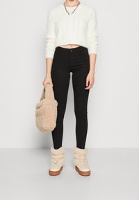 Träningströja i vitt med ribbad struktur, svarta tajta jeans, beige mjuk väska och krämfärgade stövlar med uppvikta skaft och bruna sulor.