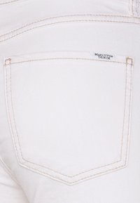 Tejido de denim blanco con un bolsillo trasero que presenta costuras en beige claro y una pequeña etiqueta que dice "Marc O'Polo DENIM."