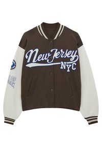 Brązowa kurtka varsity z białymi rękawami, z napisem "New Jersey" i "NYC" w niebieskim kolorze. Posiada paskowane, ściągacze przy rękawach oraz dwie przednie kieszenie.