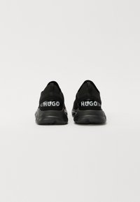 Czarne sportowe buty z teksturowaną cholewką, elastycznymi pętelkami na pięcie i kontrastowym logo "HUGO" z tyłu. Wyposażone w amortyzowaną podeszwę.