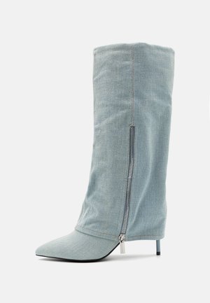 Lichtblauwe denim enkellaars met hoge hak, puntige neus en ritssluiting aan de zijkant, rechtopstaand op een witte achtergrond.