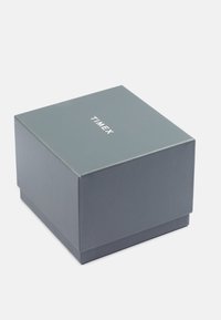 Szara tektura kartonowa o gładkiej fakturze, z centralnie umieszczonym białym logo "TIMEX" na wieczku i jednolitą szaro-skalną podstawą.
