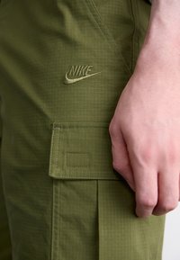 Oliņzaļi kravu bikses ar režģa tekstūru, ar Nike logo izšūtu saskaņotā diegā un sānu kabatu ar vāciņu.