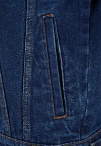 Tessuto di denim blu scuro con cuciture verticali e una tasca a filetto aperta rifinita con cuciture arancioni.