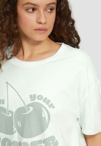 Biała koszulka z krótkim rękawem z grafika dwóch wiśni i napisem "w twojej MOCY" w szarym druku. Miękki, gładki materiał.