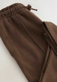 Brune joggerbukser lavet af blødt stof. Med elastisk talje med snøre, sidelommer og en glat overflade.